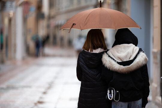 Two Female Friends Walking Together Under an Umbrella on a Rainy City Street