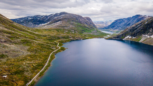 Aerial view of Djupvatnet lake surrounded by rugged mountains with patches of snow and a winding road along the shoreline in Stranda Municipality, More og Romsdal, Norway.