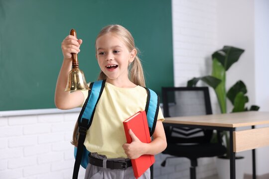 Pretty little girl with school bell and notebook in classroom