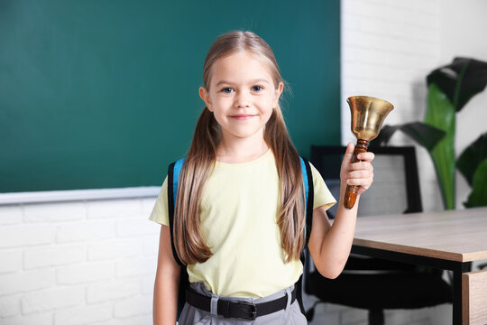 Pretty little girl with school bell in classroom