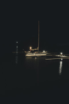 View of a sailboat moored at a dock at night, illuminated by its own lights on the dark water in Sviby, Laane County, Estonia.