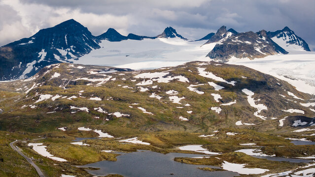 Aerial view of Sognefjellet featuring rugged mountain peaks, glaciers, alpine lakes, and a winding road in the landscape of Lom Municipality, Innlandet, Norway.