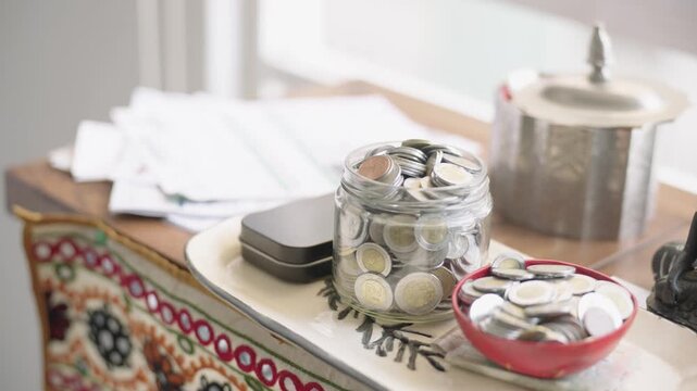Mexican pesos in a glass jar and red bowl on a tray representing savings and personal finance