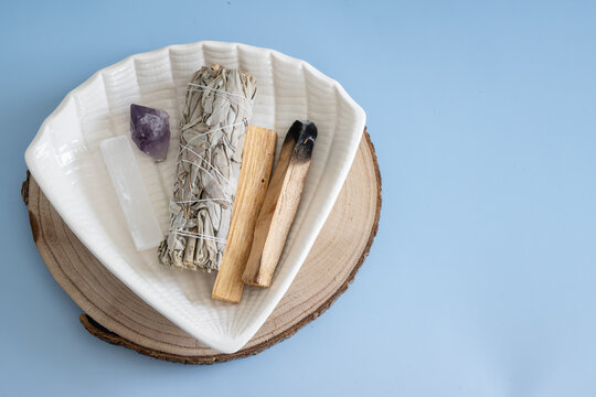 White sage smudge bundle with selenite, amethyst crystal, and palo santo wood arranged in a ceramic dish for a spiritual cleansing ritual