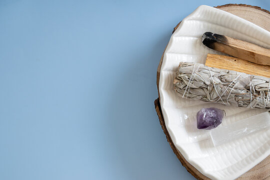 aromatherapy setup with sage bundle, amethyst, and palo santo on a blue background