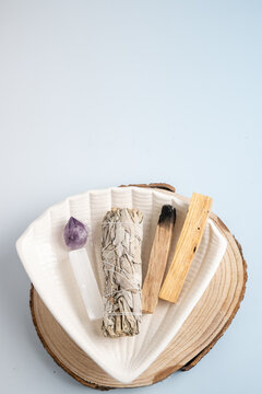 wellness ritual tools including sage, crystals, and palo santo on a light wood background