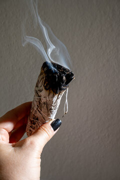 hand holding smudge stick with smoke rising against neutral background. concept of cleansing ritual.