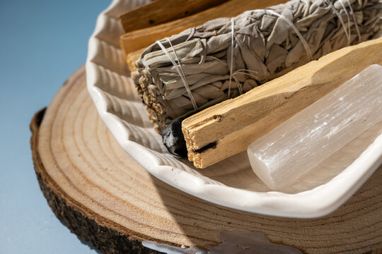 sage smudge stick, palo santo wood, and selenite crystal on wooden plate for spiritual cleansing