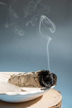 smoke rising from burning sage stick on plate creating calming atmosphere in serene setting