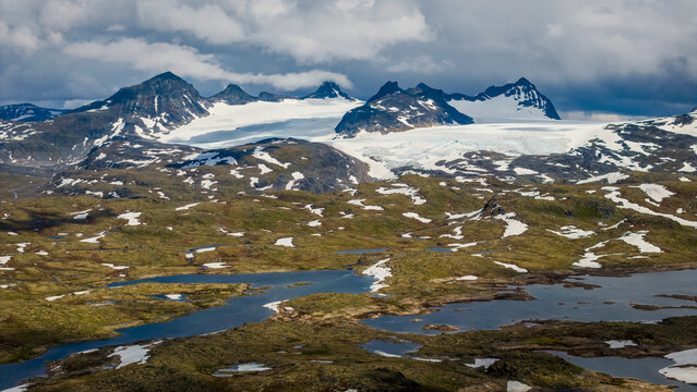 Aerial view of Sognefjellet mountain range with glaciers, snow-capped peaks, alpine lakes, and tundra landscape in Lom Municipality, Innlandet, Norway.