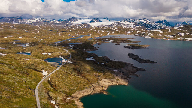 Aerial view of Sognefjellet mountain pass with a winding road, a large lake, and snow-capped peaks in Lom Municipality, Innlandet, Norway.