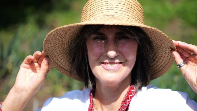 Portrait of happy ukrainian woman in traditional vyshyvanka at sunny summer day. Adult smiling lady wearing in straw hat looking into camera outdoor. Concept of national identity and patriotism
