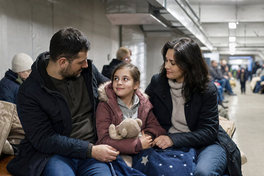 Father, mother and child sitting in underground shelter during air alarm. Family seeking safety in bunker. Humanitarian crisis, war conflict and civilian support concept.