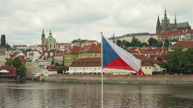 Czech national flag waving on flagpole over Vltava River in Prague. Historic Prague Castle and city skyline background. Concept of national symbol, patriotism, European travel, and culture.