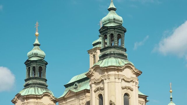 St. Nicholas Church towers with green copper domes stand in Old Town Square in Prague. Historic baroque church architecture features ornate details for travel and cultural heritage concepts.