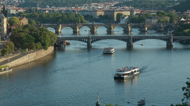 Tourist ships sail on Vltava River near historic bridges in Prague. Excursion boats carry passengers along scenic waterways. European travel destination for summer vacation and city tourism.