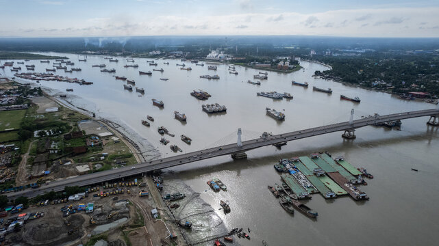 Aerial view of the Karnaphuli River with numerous cargo ships, a large bridge, and industrial port facilities along the banks in Chittagong, Chittagong Division, Bangladesh.