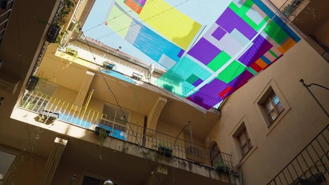 Colorful fabric canopy stretches over an inner residential courtyard to provide sun shade. Vibrant textile awning decorates the outdoor building patio. Perfect for urban lifestyle concepts.