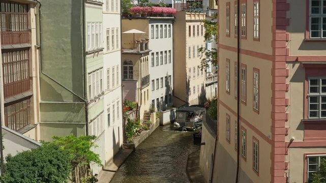 Small tourist boat sails through narrow Certovka canal between historic buildings in Prague. Scenic water channel view in Mala Strana district for European travel and city tourism.