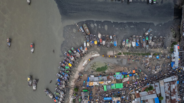 Aerial view of the busy fish yard in Chittagong, featuring numerous wooden fishing boats moored along the muddy riverbank and bustling market activity. Chittagong, Chittagong Division, Bangladesh.
