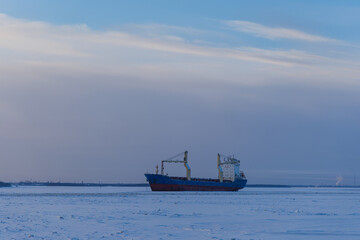 Minimalist arctic landscape with cargo vessel locked in frozen river ice under winter sky with copy space. Maritime shipping and transport logistics. © Konstantin