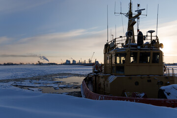 Close up of tugboat wheelhouse near open water in frozen river ice with port background. Arctic maritime transport and industrial shipping logistics. © Konstantin