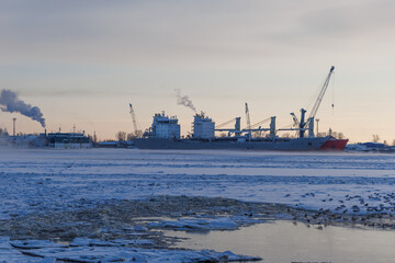 Large cargo vessel locked in frozen river ice with seagulls near open water lane. Winter arctic industrial landscape with copy space. © Konstantin