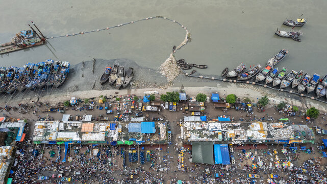 Aerial view of the busy Fish Yard with fishing boats docked along the riverbank, market stalls, and crowds of people in Chittagong, Chittagong Division, Bangladesh.