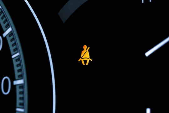speedometer on black background. Close up of illuminated seat belt warning light on car dashboard, safety alert indicator reminding driver and passengers to fasten seat belts while driving