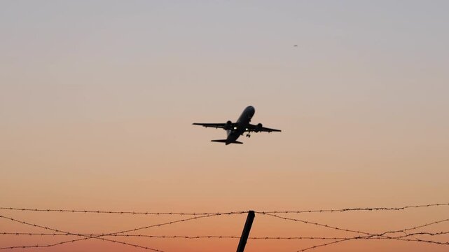 Commercial passenger airliner taking off at sunset behind a fence