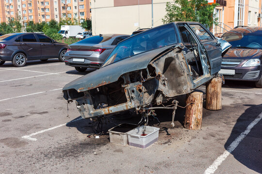 Stripped car body in residential parking, damaged abandoned vehicle, theft and urban crime.