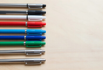 Fototapeta premium Assortment of colorful ballpoint pens and silver pens arranged neatly on a light wooden desk surface with copy space