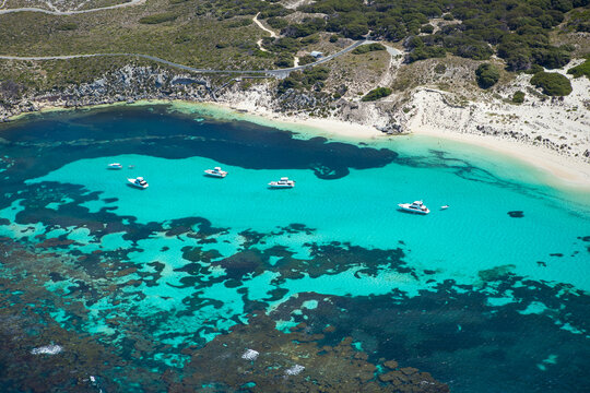 Aerial view of Parker Point with turquoise water, coral reefs, white sand beach, and boats anchored in the bay in Rottnest Island, Western Australia, Australia.