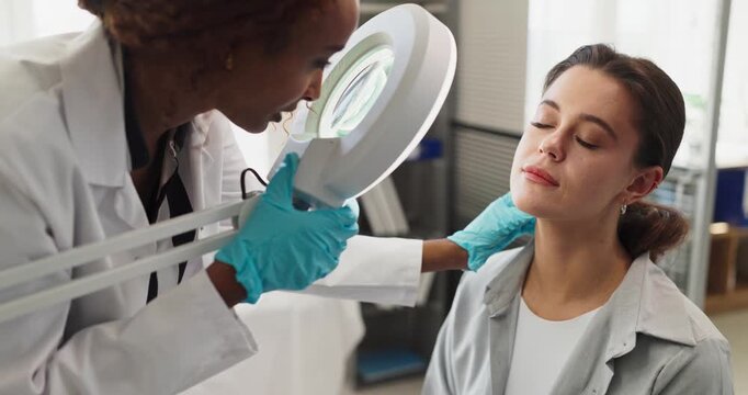 Dermatologist doctor examines patient woman with magnifier. Professional skin examination in a modern clinic during healthcare consultation. Clean safe medical skincare service concept.