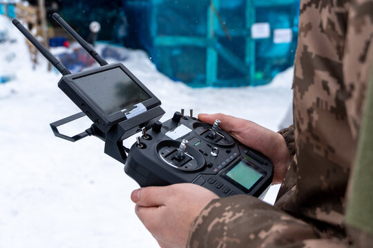 Person in military uniform holding an FPV drone controller in the snow