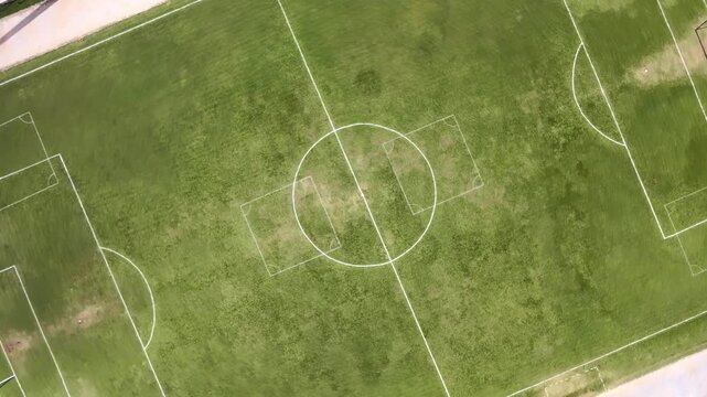 High angle aerial drone view flying over a green football field with marked white lines