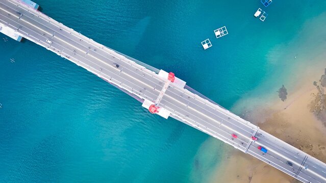Aerial view of Jembatan Merah Putih spanning over turquoise waters with small structures in the sea in Kecamatan Sirimau, Maluku, Indonesia.