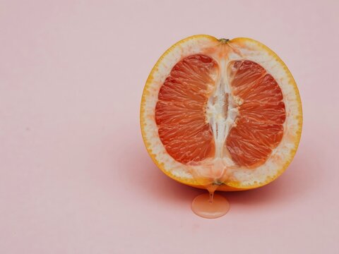 Fresh halved grapefruit with dripping juice on a soft pastel pink background