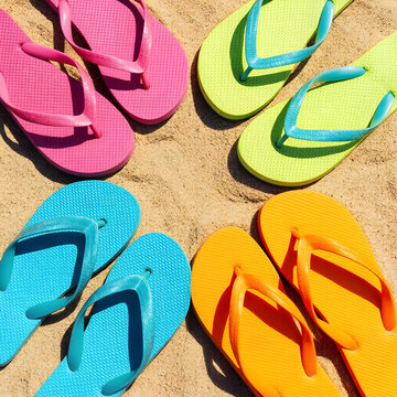 Four pairs of colorful flip flops on a sandy beach, summer vacation and travel footwear, top down view
