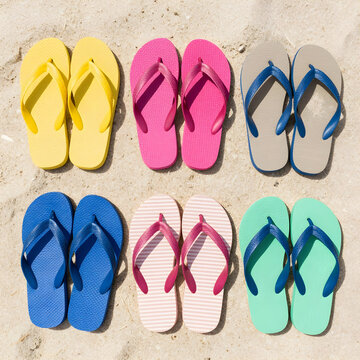 Multiple colorful flip flops arranged in rows on a sandy beach, summer vacation and travel footwear