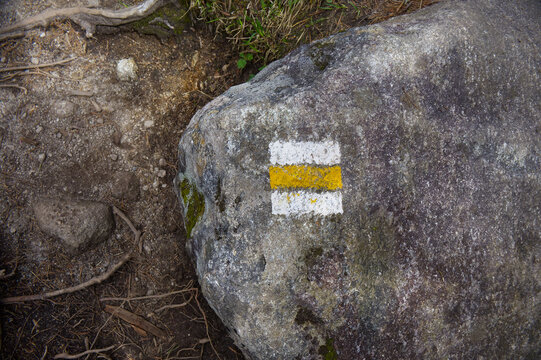 Yellow and white painted tourist hiking trail sign marker on a rough stone surface. Navigation symbol for outdoor trekkers and mountaineers in wilderness.