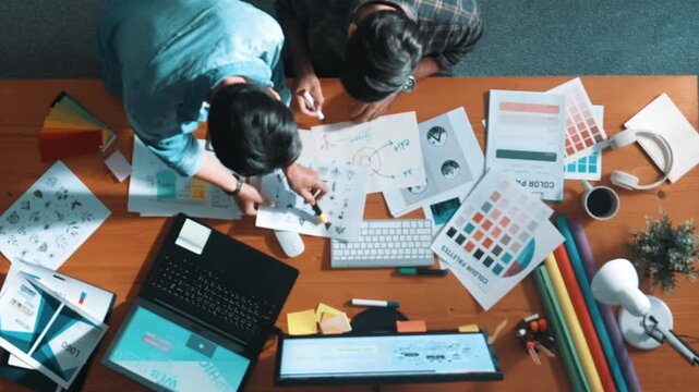 Top down view of smart designer helping manager choosing color from colored palettes. Aerial view of businessman working together and planning together while looking at logo from laptop. Symposium.