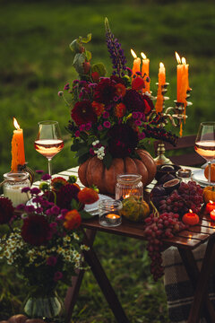 Cozy autumn table decoration for a thanksgiving party outdoors. Grapes, fig, rose wine, candles, pumpkins as decor. Elegant wedding fall arrangement, beautiful setting for a romantic proposal