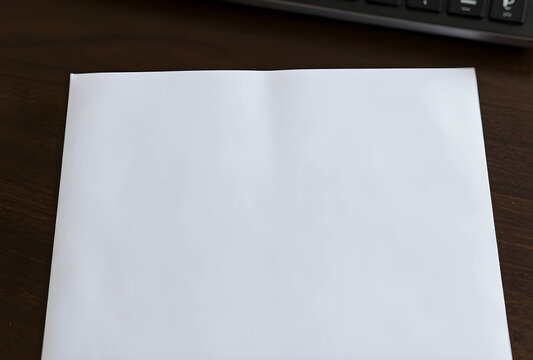 Blank white paper sheet on a dark wooden desk with a keyboard in the background, ready for text or design, a black computer keyboard is partially visible in the background