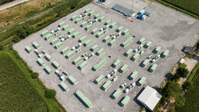 Aerial view of BESS SERRE TAVAZZANO, a battery energy storage system facility with rows of green containers on a gravel lot in Tavazzano con Villavesco, Lombardy, Italy.