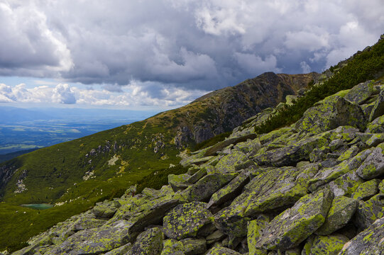 Epic alpine landscape with lichen-covered rocks in foreground, a tarn, and deep valley in the High Tatra Mountains.