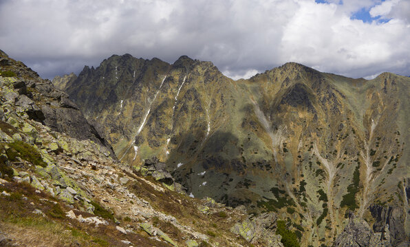 Dynamic lighting with cloud shadows moving across the steep, rocky ridges and rugged peaks of the High Tatras mountains on a summer day.