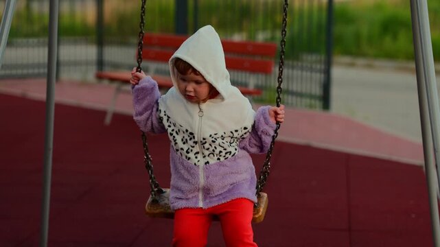 Child enjoying a swing at an outdoor playground, gripping the chains and moving through a playful moment of childhood recreation