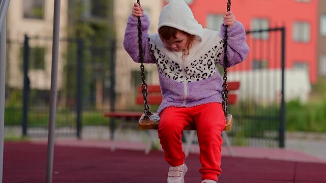 Child enjoying a swing at an outdoor playground, gripping the chains and moving through a playful moment of childhood recreation