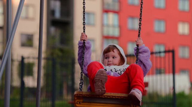 Child enjoying a swing at an outdoor playground, gripping the chains and moving through a playful moment of childhood recreation